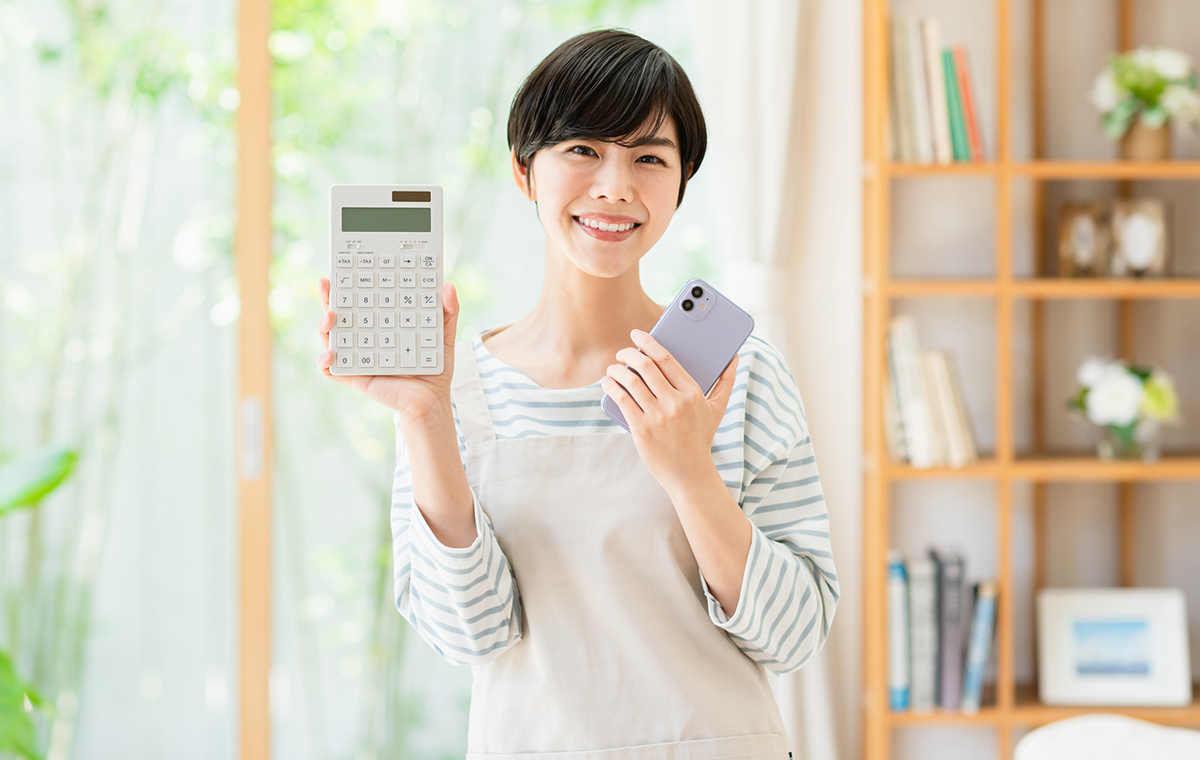 電卓とスマートフォンを手に笑顔を見せるエプロン姿の女性